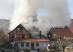 Gewaltige Rauchwolken steigen aus mehreren brennenden Häusern in der Wernigeröder Innenstadt am Montag (23.01.2006), während Feuerwehrleute mit Drehleitern bei den Löscharbeiten sind. (Foto: dpa)