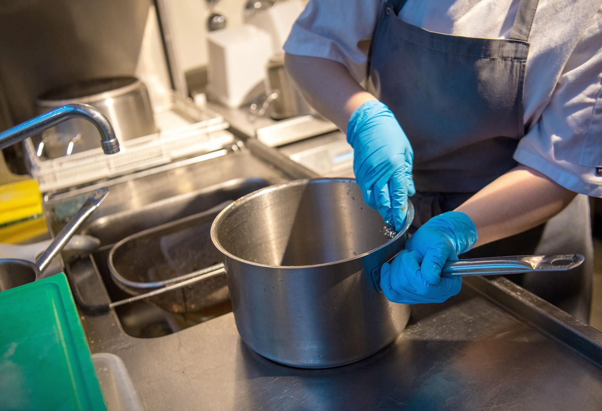 Eine Küchenhilfe spült einen Topf in einem Restaurant