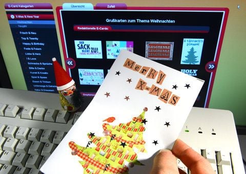 Ein Mann hält eine Weihnachtskarte vor einen Computerbildschirm, auf dem eine Internetseite für elektronische Weihnachtskarten zu sehen ist. (FOTO: DPA)