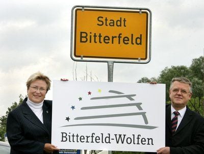 Petra Wust und Helmut Kraußer, stehen mit einem Logo am Ortseingangsschild von Bitterfeld. (FOTO: DPA)
