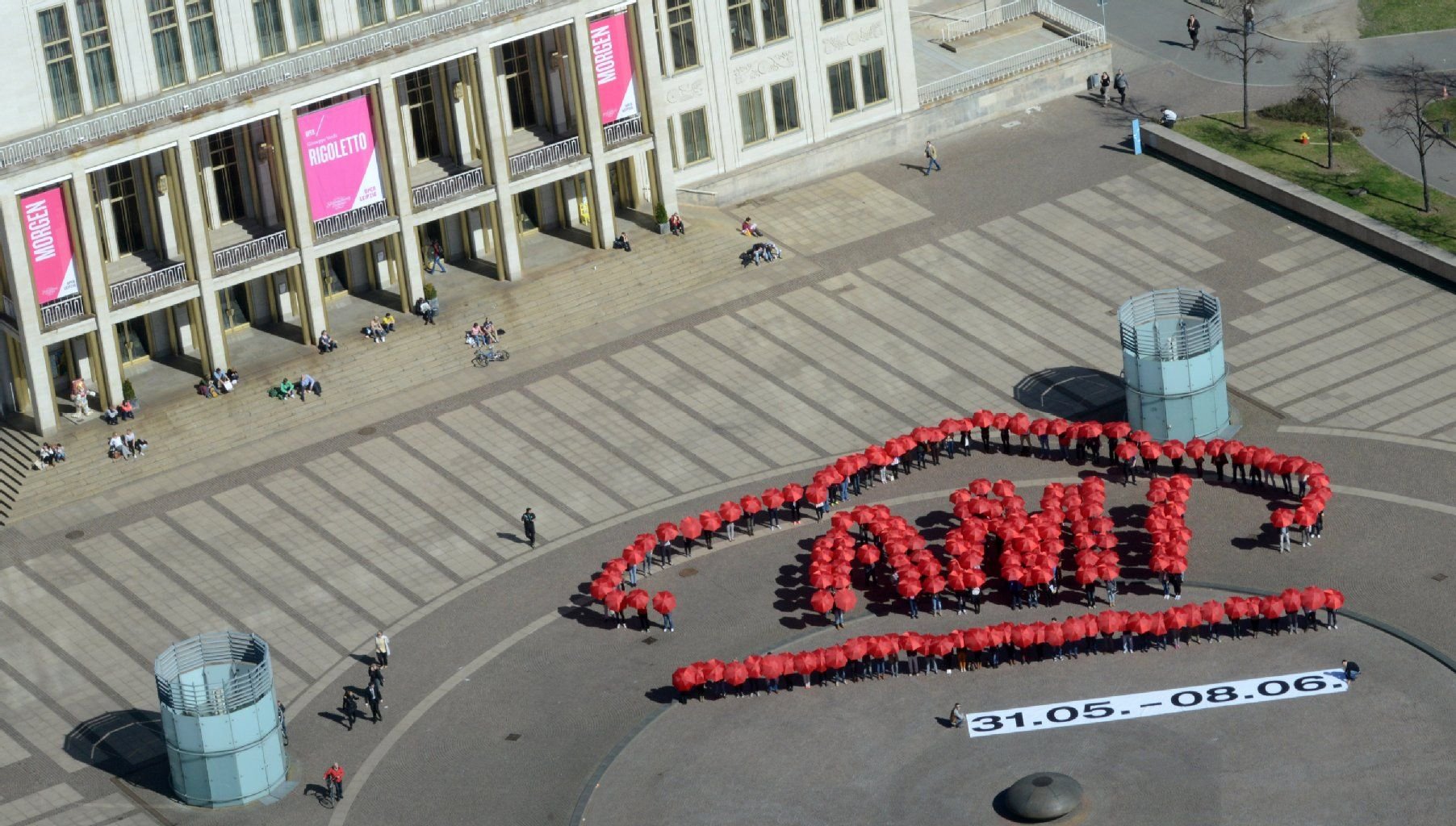 Über 180 Mitwirkende mit roten Regenschirmen gestalten das Logo der Automobilmesse AMI auf dem Augustusplatz in Leipzig (Sachsen).