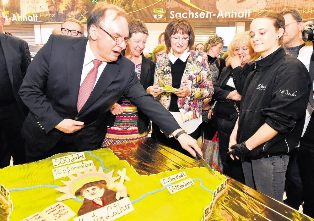 Ministerpräsident Reiner Haseloff schneidet im Beisein von Agrarministerin Claudia Dalbert (zweite von links) eine Luther-Torte in der Form der Landesgrenzen von Sachsen-Anhalt an.