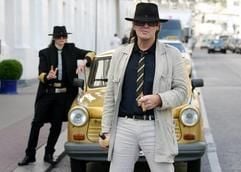 Udo Lindenberg steht am Dienstag (9. Mai) vorm Hotel «Atlantic» in Hamburg zusammen mit seinem Double Sven Martens (l.) mit einer Zigarre und einer Flasche Eierlikör vor seinem goldenen Trabant 444. (Foto: dpa)