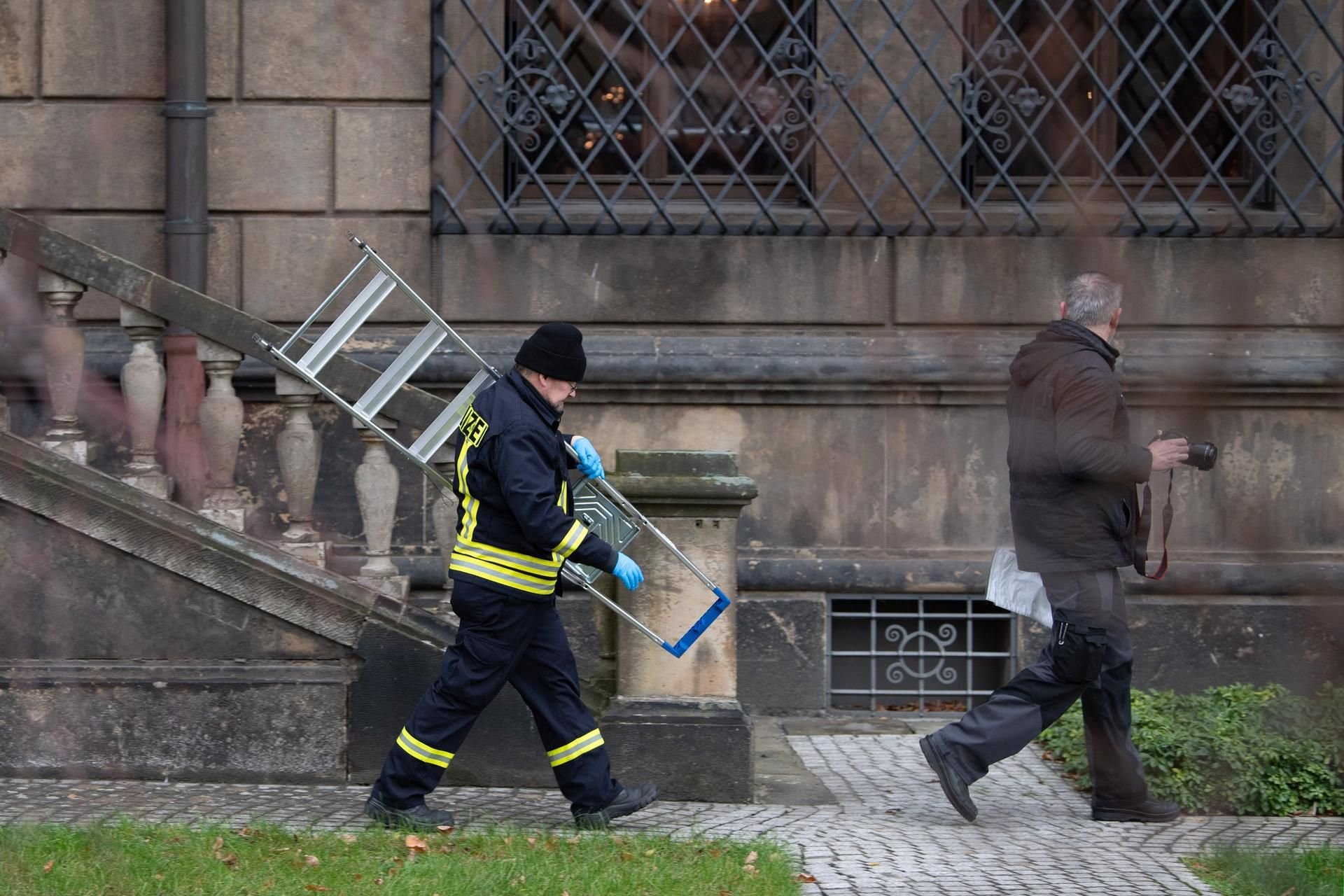 Einsatzkräfte der Polizei gehen mit einer Leiter im Bärengarten vor den Gitterfenstern des Grünen Gewölbes am Residenzschloss in Dresden entlang.