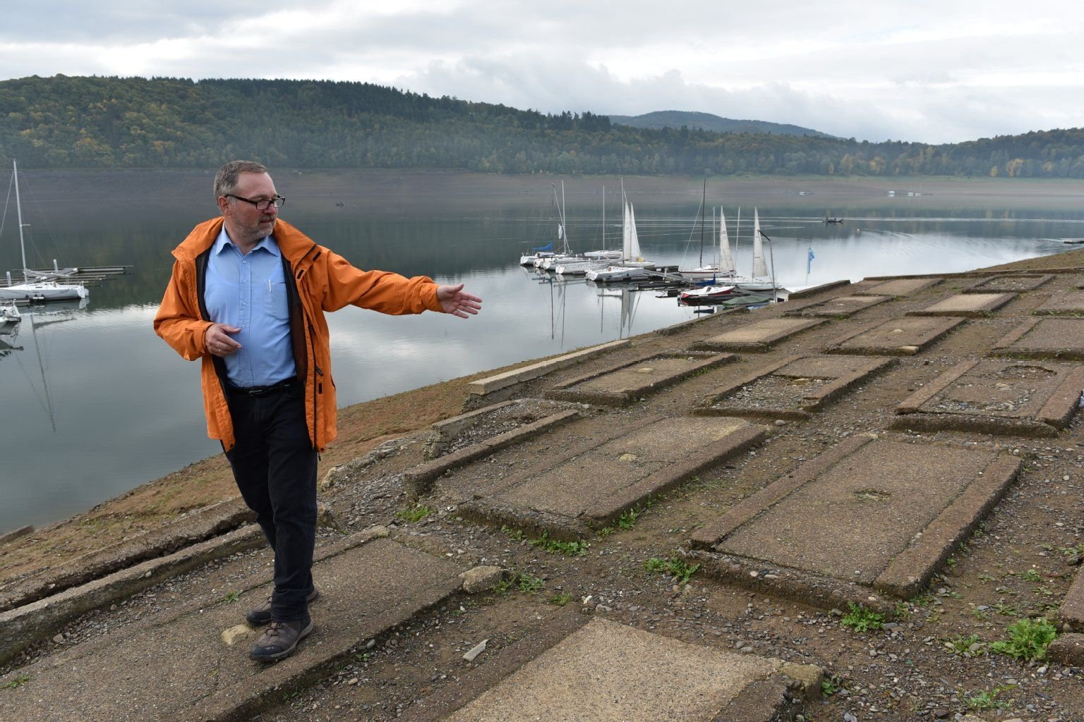 Uwe Neuschäfer vom Förderverein zum Erhalt der Dorfstelle Berich steht auf den Überresten des Friedhofs der Dorfstelle Berich am Edersee bei Waldeck (Hessen) und den mit Betonplatten gesicherten Gräbern.