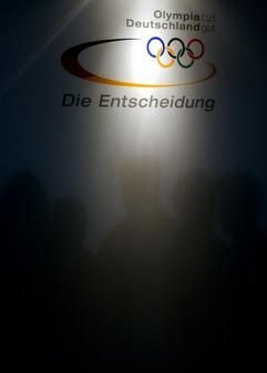 Die Schatten von fünf Personen fallen am Freitag (11.04.2003) in München unter das Logo für die Olympia-Bewerbung 2012. Am Samstag (12.04.2003) wählen die Mitglieder des Nationalen Olympischen Komitess (NOK) die Bewerber für die Olympischen Sommerspiele 2012. Kandidaten für die Sommerspiele in neun Jahren sind die Städte Düsseldorf, Frankfurt, Hamburg, Leipzig und Stuttgart. Das Ergebnis wird NOK-Präsident Steinbach zusammen mit Bundeskanzler Gerhard Schröder verkünden. (Foto: dpa)