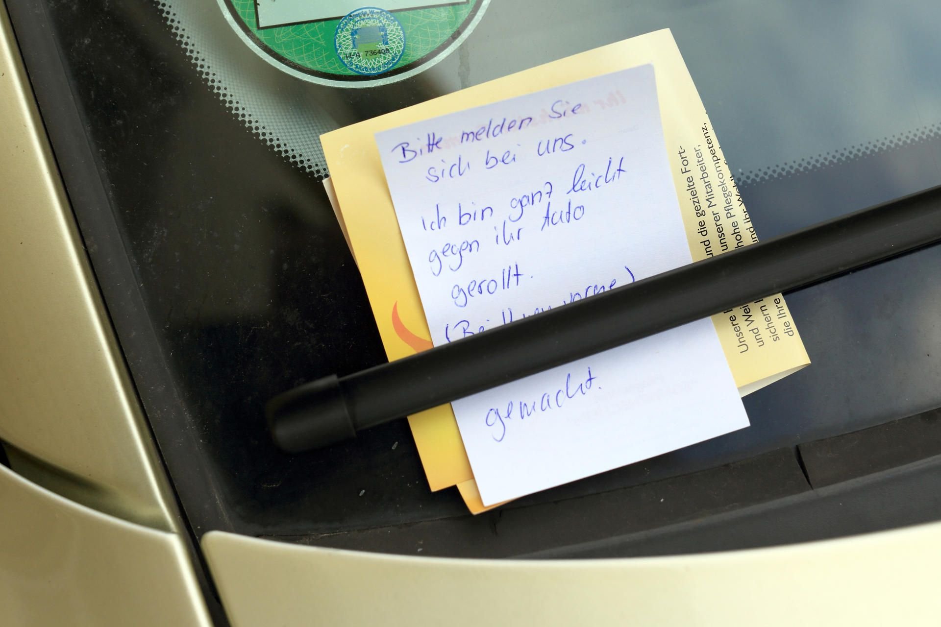 Ein Zettel mit der Aufschrift: "Bitte melden Sie sich bei uns. Ich bin ganz leicht gegen ihr Auto gerollt", klemmt an einem PKW hinter einem Scheibenwischer.