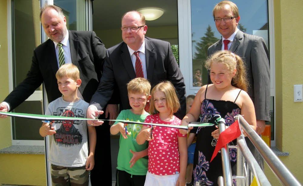 OB Andreas Michelmann (l.), Staatssekretär Jörg Felgner und Landrat Markus Bauer (r.) schneiden mit den Kindern das Band durch.