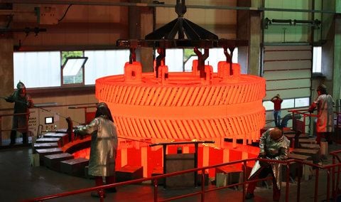 Arbeiter in Schutzanzügen manoevrieren in der Harms Lohnhaerterei GmbH in Magdeburg ein glühendes Zahnrad aus einem Brennofen. (FOTO: DAPD)