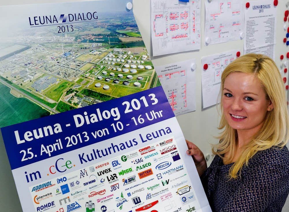Kriistin Sander präsentiert das Plakat zur achten Standortmesse „Leuna Dialog“ am 25. April.