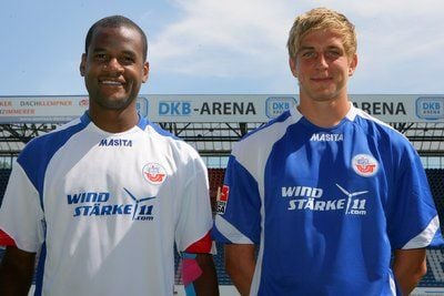 Die Spieler des Fußball-Zweitligisten FC Hansa Rostock, Orestes (l) und Bastian Oczipka, präsentieren auf einer Pressekonferenz in Rostock das Trikot mit dem neuen Hauptsponsor «Windstärke11».