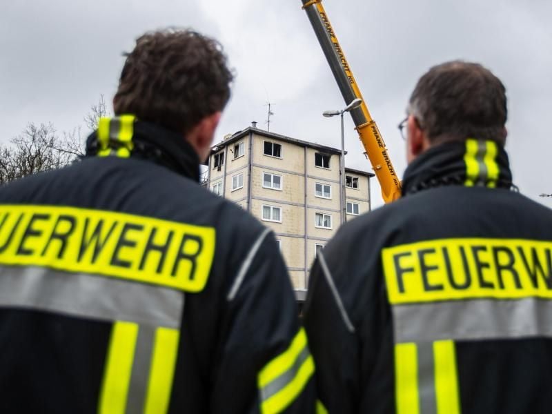 Zwei Feuerwehrmänner blicken auf ein ausgebranntes Hochhaus. Foto: Guido Kirchner/dpa/Archivbild