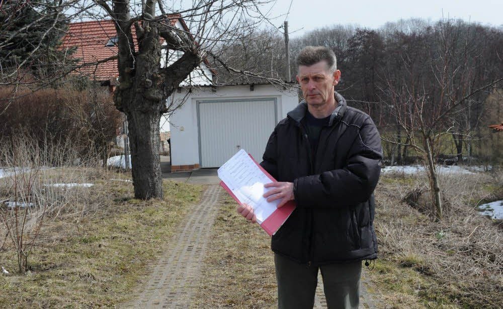 Bodo Adam versteht die Welt nicht mehr: Er weiß nicht, wie er den Abwasseranschluss zu seinem Haus (Hintergrund) begleichen soll.