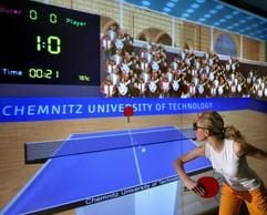 In einem Virtual-Reality-Labor der TU Chemnitz testet die Studentin Grit Henoch am Dienstag (31.01.2006) eine an der Universität entwickelte Tischtennis-Simulation. Die virtuelle Spielumgebung, wie Tischtennisplatte mit Netz und Zuschauertribüne werden durch eine Rückprojektion auf eine Großbild-Leinwand erzeugt. Für derartige Simulationen extrem schneller Bewegungen entwickelten Forscher der Professur Graphische Datenverarbeitung und Visualisierung spezielle Vorhersageberechnungen, welche die hard- und softwarebedingten Verzögerungszeiten weitgehend kompensiert. Erstmals wird das neue System im März auf der weltgrößten Computermesse CeBIT in Hannover vorgestellt. (Foto: dpa)