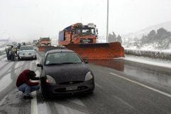 Autofahrer ziehen auf einer Straße nahe Athen Schneeketten auf die Räder ihrer Fahrzeuge, während ein Schneepflug die Straße räumt. (Foto: dpa)