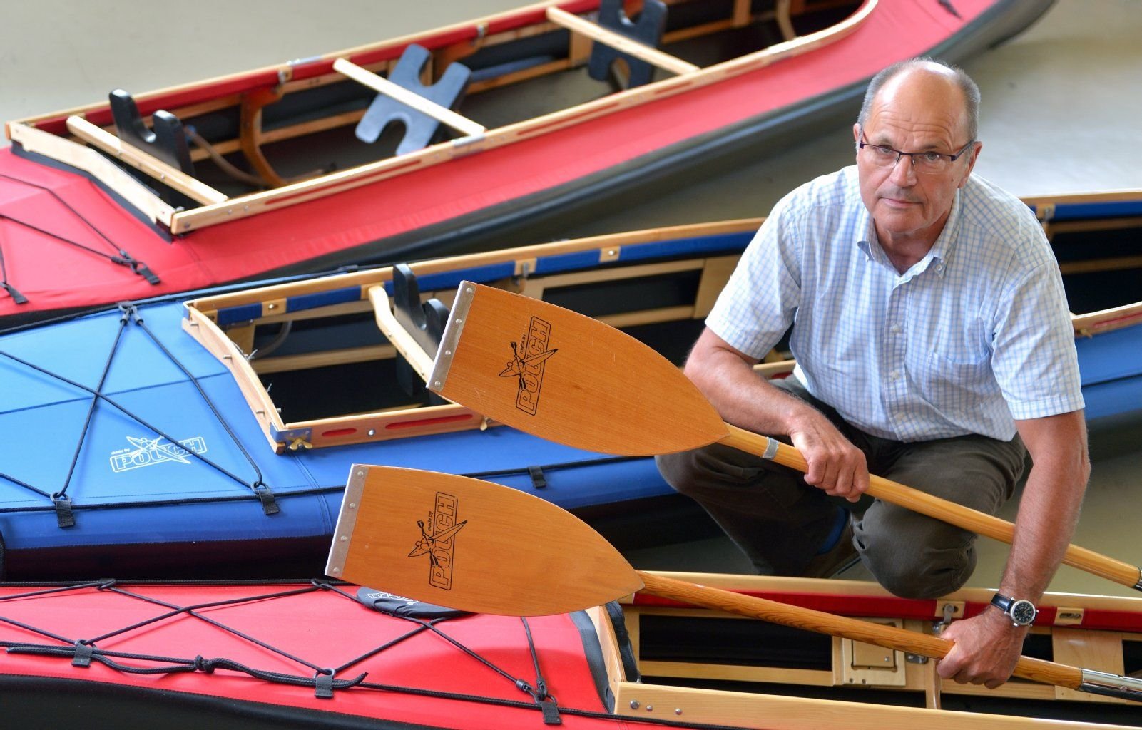 Der Geschäftsführer der Poucher Boote GmbH, Ingolf Nitschke, kniet zwischen drei Booten in seinem Geschäft in Pouch.