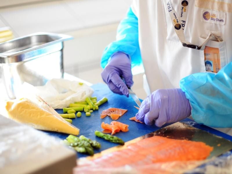 Ein Mann fertigt Mahlzeiten aus Lachs und grünem Spargel in der Produktion der LGS Sky Chefs. Foto: Daniel Reinhardt/dpa/Archivbild