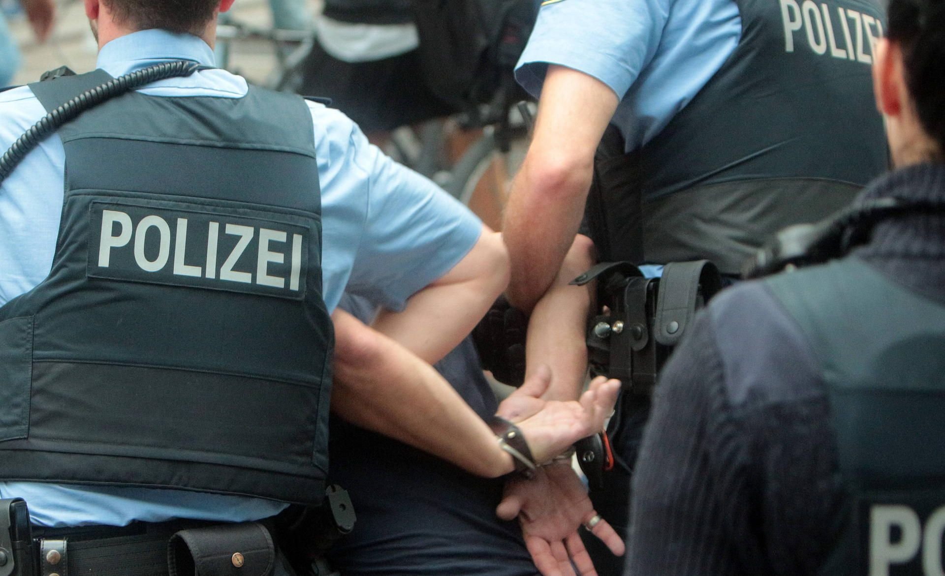 Polizisten führen einen Widerstand leistenden Täter in Handschellen ab.