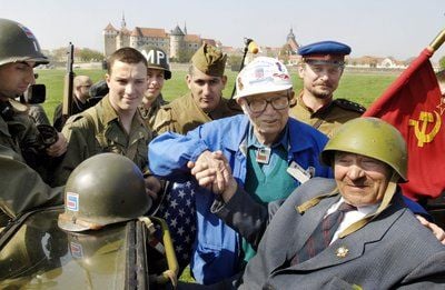 Mit einem Händedruck erinnern im April 2005 der Weißrusse Alexander Silwaschko (r.) und der Amerikaner E.A. Bud Parsons (3.v.r.) in Anwesenheit von französischen Soldaten vor der Kulisse von Torgau an der Elbe an das Kriegsende 1945. (FOTO: DPA)