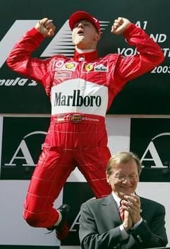 Der deutsche Formel 1-Weltmeister Michael Schumacher (Ferrari) macht am Sonntag (18.05.2003) auf dem A1-Ring in Spielberg/Österreich nach seinem Sieg beim Großen Preis von Österreich auf dem Podium einen Freudensprung. Im Vordergrund applaudiert der österreichische Bundeskanzler Wolfgang Schüssel. Schumacher siegte vor dem Finnen Kimi Räikkönen und dem Brasilianer Rubens Barrichello. (Foto: dpa)