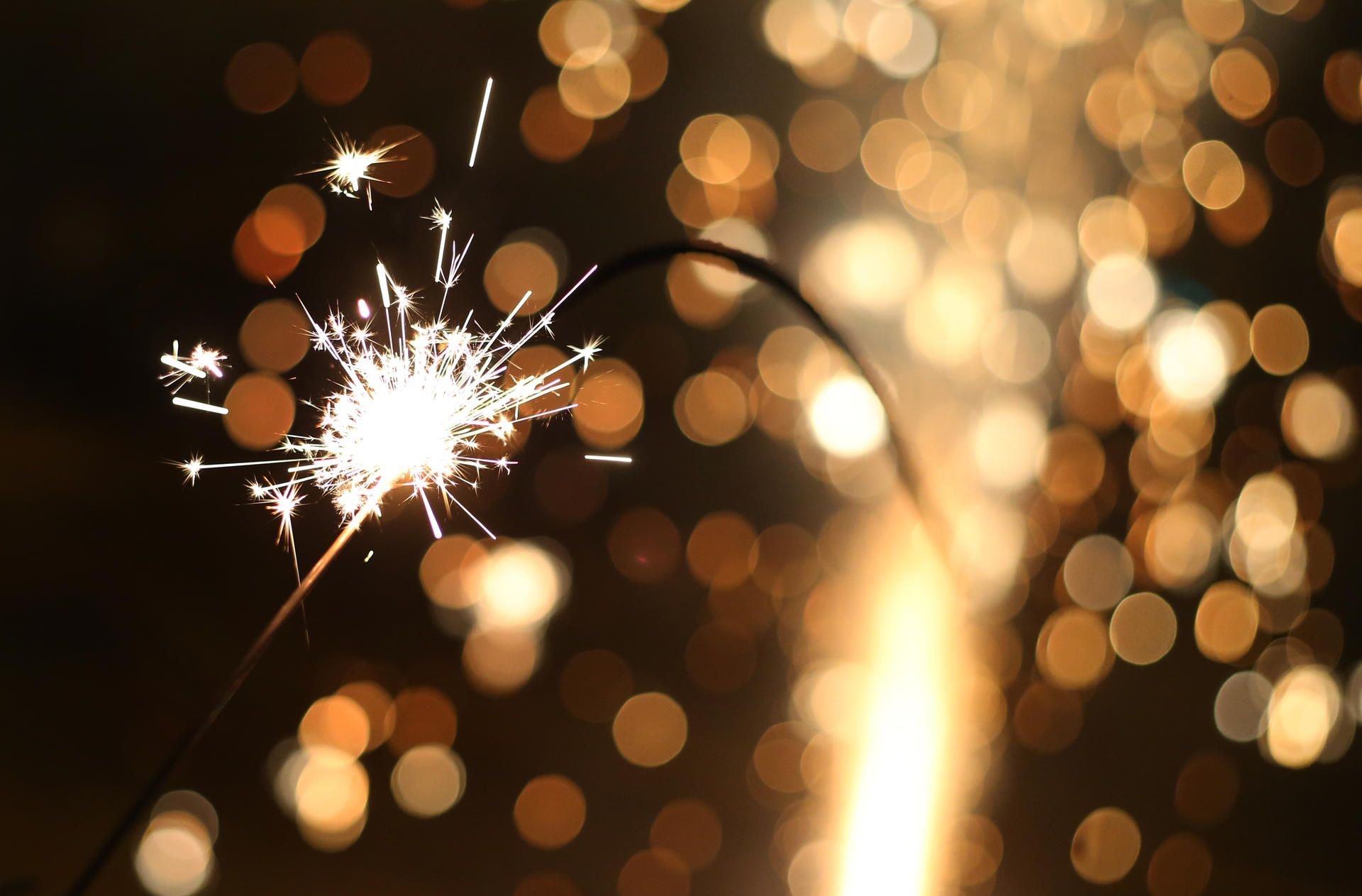 Ein Kind hält eine brennende Wunderkerze vor einem gezündeten Silvesterfeuerwerk.