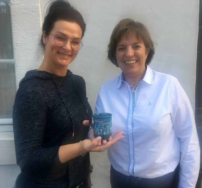 Nicole Bösener (li.) und Christina Lahne präsentieren die Halli-verzierte Glühweintasse zum Weihnachtsmarkt am Kugelbrunnen.