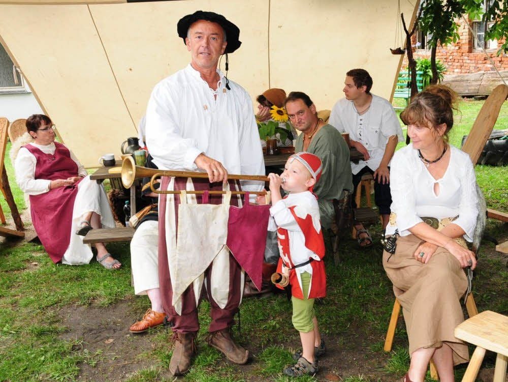 Knappe Edgar gibt auf dem Klödener Burghof mit dicken Backen das Fanfarensignal „Fertig machen zum Turnier!“. Hofmarschall Ingolf unterstützt den Nachwuchsbläser dabei.