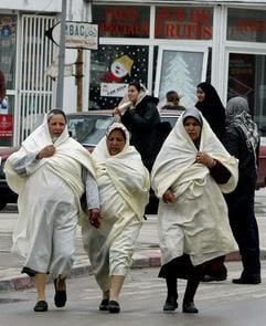 Frauen in traditioneller Kleidung laufen in Monastir in Tunesien über eine Straße. (Foto: dpa)