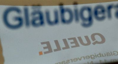Auf dem Schild mit der Aufschrift "Gläubigerausschuss" spiegelt sich vor Beginn der Gläubigerversammlung der Quelle-Schriftzug. (FOTO: DPA)