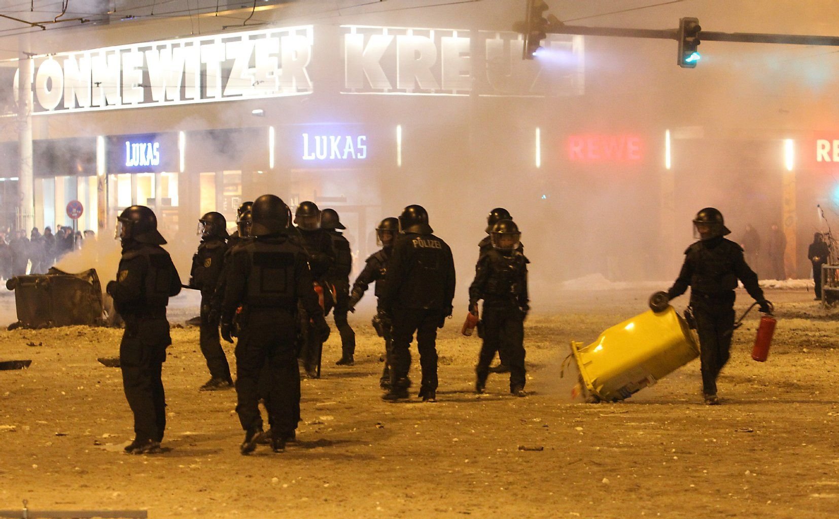 Polizisten stehen am 29.12.2014 in Leipzig (Sachsen) an umgekippten Müllcontainern. Im Anschluss an eine Schneeballschlacht mit mehreren hundert Teilnehmern im Leipziger Stadtteil Connewitz war es zu Ausschreitungen gekommen.