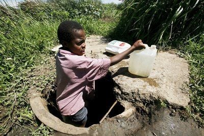 Ein jungen Simbabwer nimmt mit einem Kanister in Glen View, einem Vorort von Harare, Wasser aus einem ungesicherten Wasserloch. (FOTO: DPA)