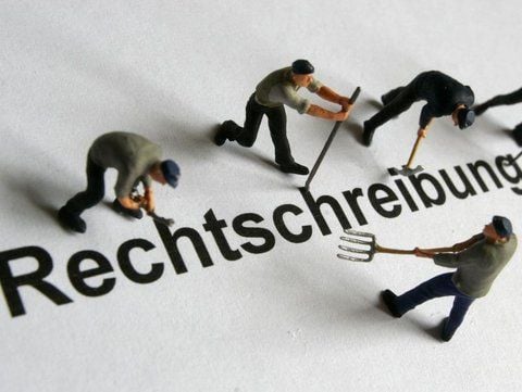 Modelleisenbahnfiguren machen sich an dem Wort «Rechtschreibung» zu schaffen.
