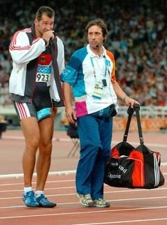 Lars Riedel (l.) verlässt am Montag (23. August 2004) nach seiner Verletzung beim Diskuswerfen das Stadion in Athen. Der Deutsche hatte zu disem Zeitpunkt an achter Stelle gelegen. (Foto: dpa)