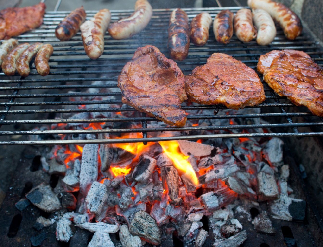 Bratwürste und Steaks liegen auf einem Holzkohlegrill.