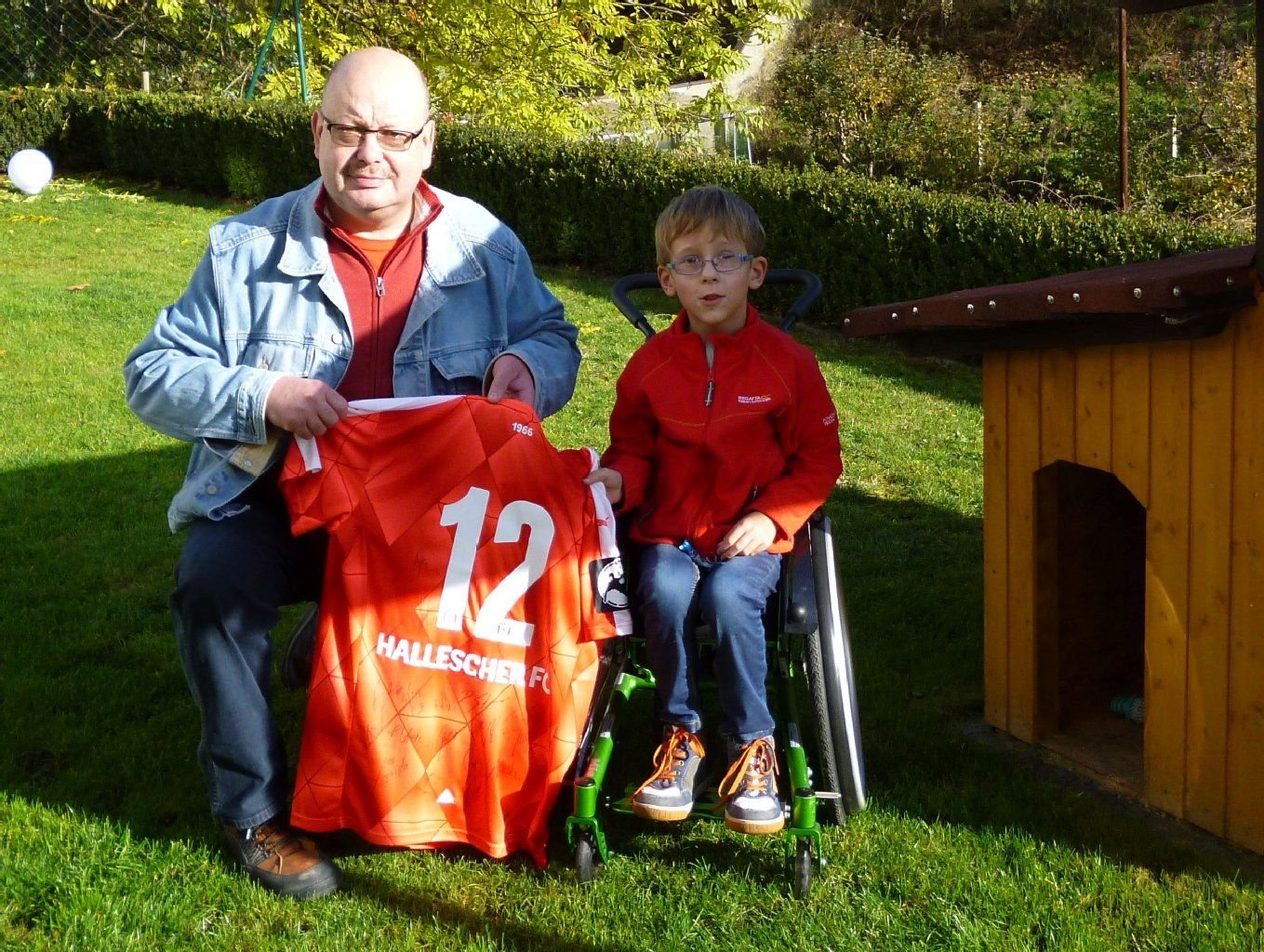 Hilfe vom HFC: Initiator Frank Wagner (l., HFC-TV) versteigert ein von der Mannschaft unterschriebenes Trikot, um dem kleinen Hugo (r.) zu helfen.