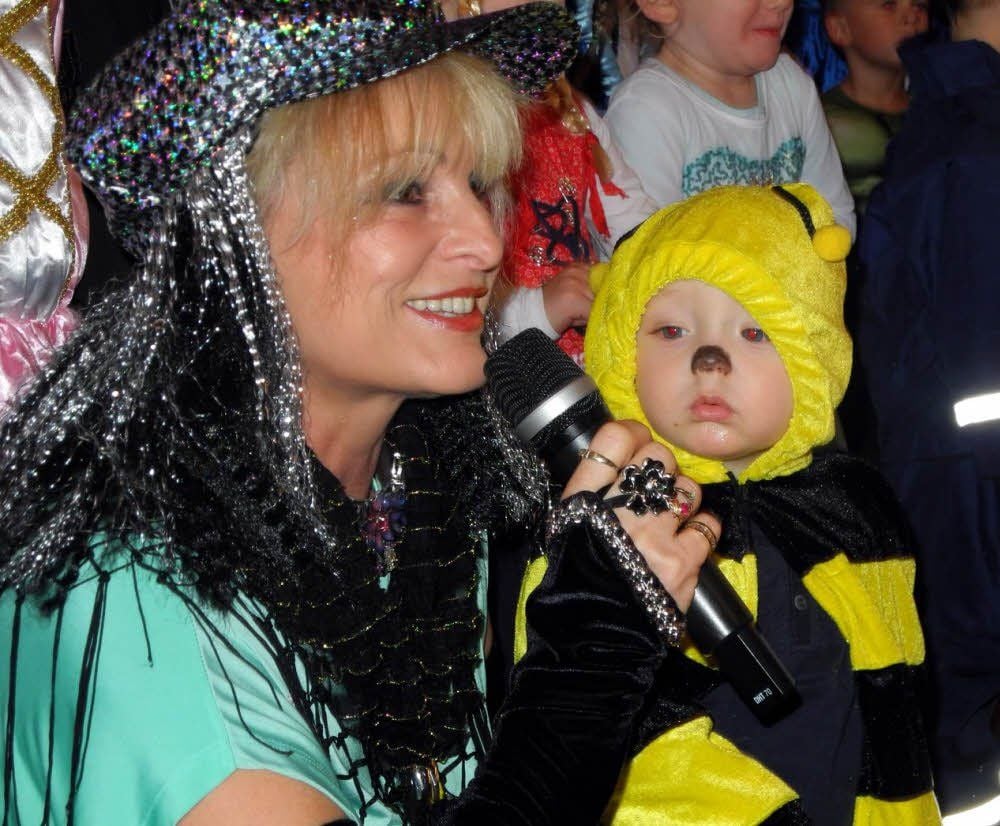 Moderatorin Antje Berger erklärt in Mönchenhöfe dem Jüngsten: „Schau Arne, das ist Fasching. Alle sind quietschvergnügt, und wir stiften sie dazu an!“