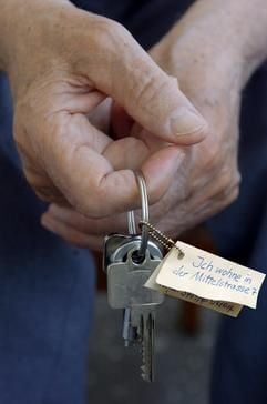 Das gestellte Foto zeigt Hände eines älteren Menschen mit einem Schlüsselbund, an dem ein Papier mit der Anschrift angebracht ist. (Foto: dpa)