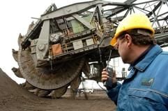 Ein Mann mit einem Funkgerät steht neben einem Bagger der Mitteldeutschen Braunkohlengesellschaft Mibrag. (Foto: dpa)