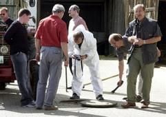 Polizeibeamte untersuchen am Dienstag (06.05.2003) im niederbayerischen Passau die Öffnung einer Grube. Bei einem tragischen Unglück ist eine ganze Familie in einer ehemaligen Hauskläranlage ertrunken. Ein 20 Monate alter Junge war nach Polizeiangaben in die etwa 75 Zentimeter breite Öffnung der Grube gefallen, während seine Eltern am Montagabend daraus Wasser schöpften. Bei dem Versuch, ihr Kind zu retten, kamen der 47-jährige Vater und seine fünf Jahre jüngere Frau ums Leben. (Foto: dpa)