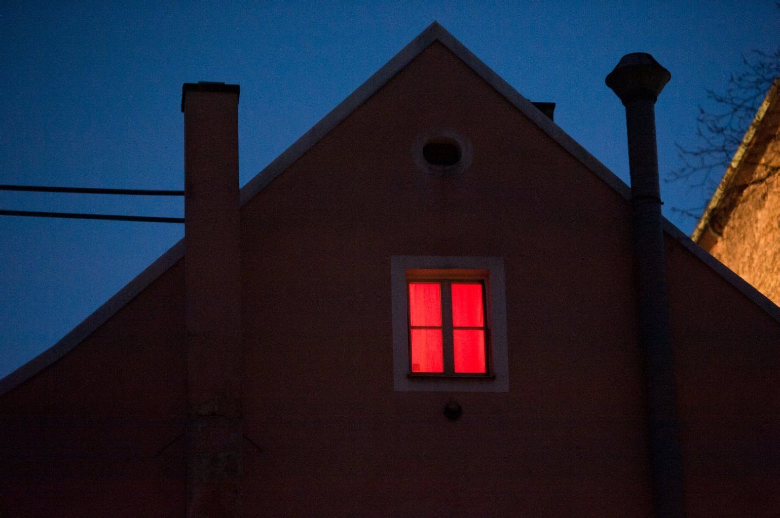 Rot leuchtet ein Fenster am Abend in einem Haus.