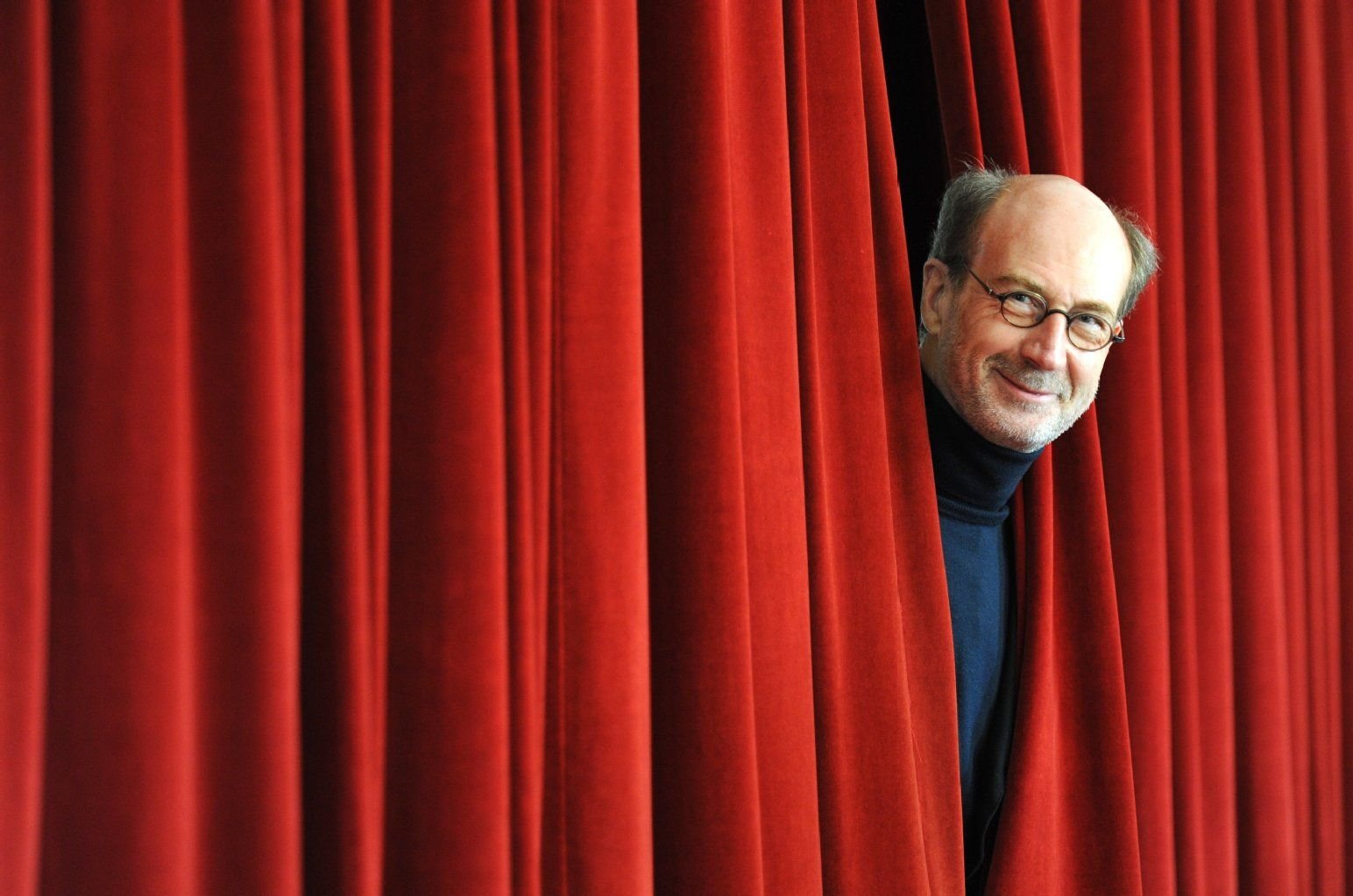 Der Geschäftsführende Direktor des Deutschen Bühnenvereins, Rolf Bolwin, schaut im Deutschen Schauspielhaus in Hamburg nach einer Pressekonferenz zwischen einem Theatervorhang hervor.