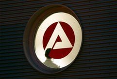 Hinter einem Fenster mit dem Logo der Agentur für Arbeit steht ein Mann im Treppenhaus der Agentur in Gelsenkirchen. (Foto: dpa)