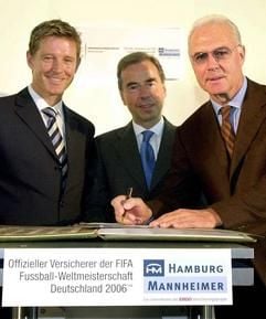 Der Präsident des Organisationskomitees der Fußball-Weltmeisterschaft 2006, Franz Beckenbauer (r), und der Vorstandsvorsitzende der "Hamburg-Mannheimer", Götz Wricke (M), unterschreiben am 8.10.2002 nach einer Pressekonferenz in Hamburg neben "Herrn Kaiser" (l, Nick Wilder) einen Kooperationsvertrag. (Foto: dpa)