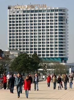 Spaziergänger flanieren auf der Uferpromenade des Ostseebades Warnemünde vor dem Fünf-Sterne-Hotel Neptun.