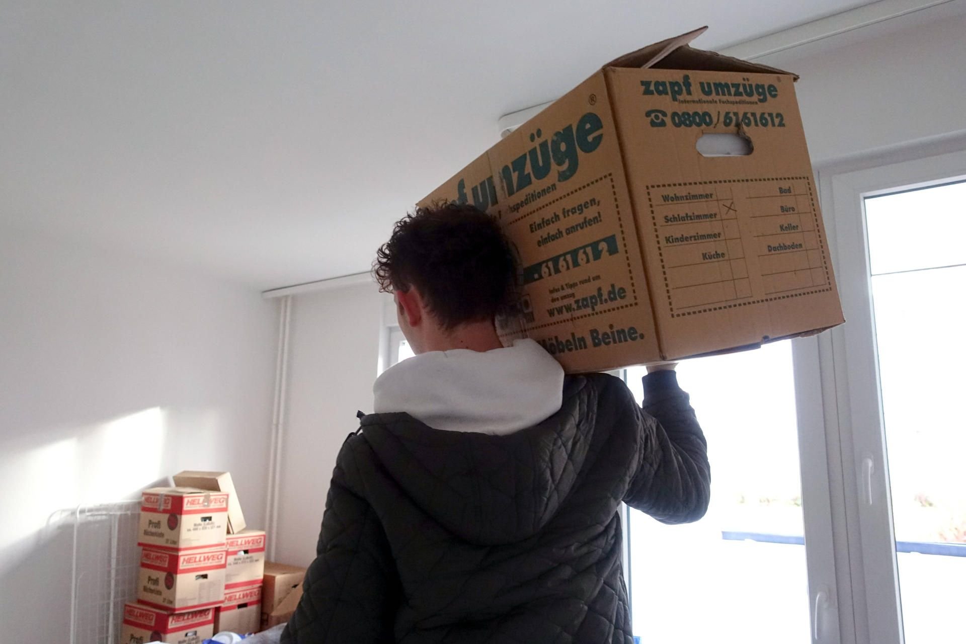 Ein junger Mann trägt einen Umzugskarton
