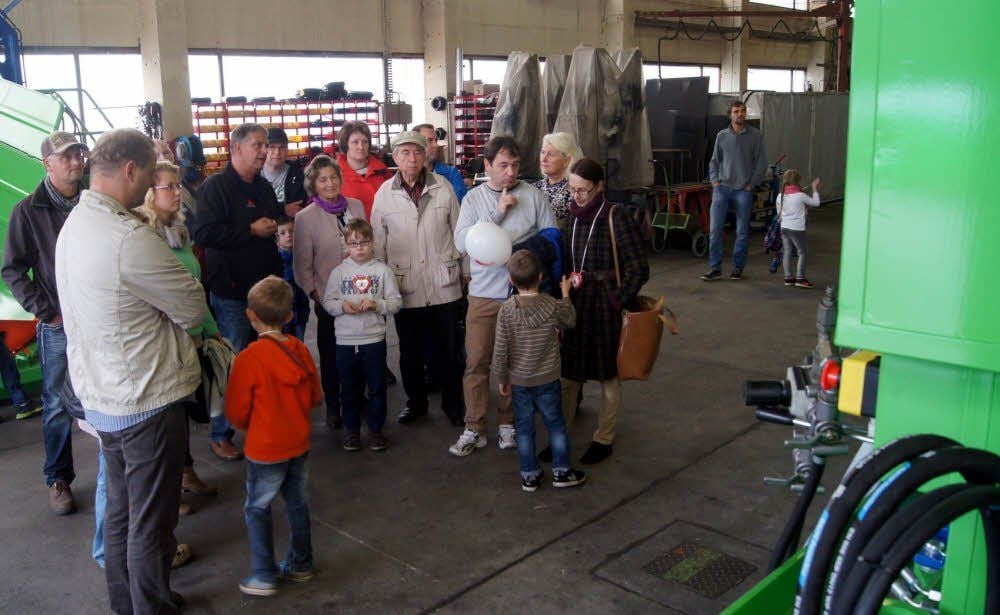 Jörg Schubert (in dunkler Jacke) erklärt einer Gruppe Besucher des Tages der offenen Tür in einer Produktionshalle ausgestellte Exponate.