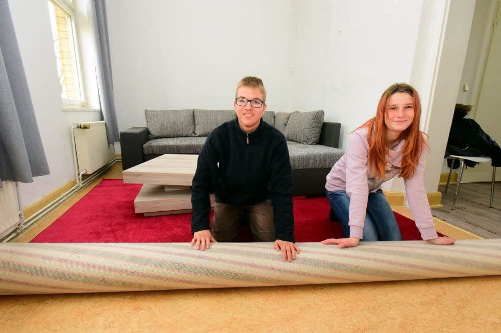 Vivien und Florian rollen in der Trainingswohnung einen Teppich aus.