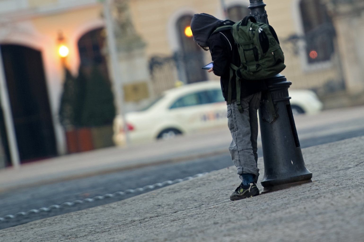 Ein Schulkind mit Schulrucksack steht angelehnt an einer Straßenlampe.