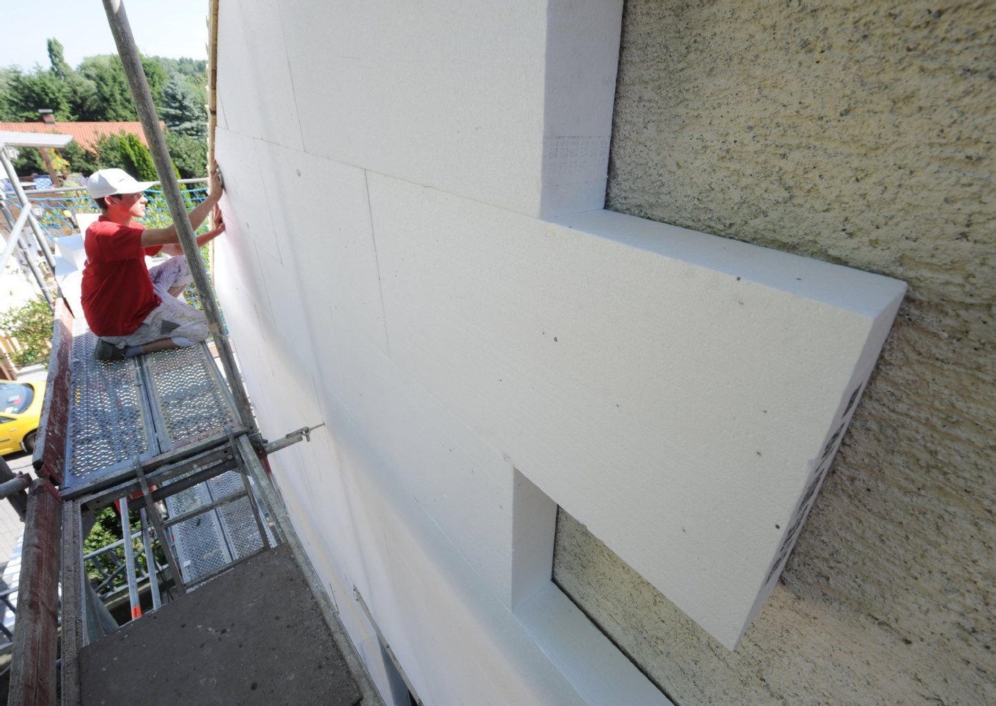 Ein Fachmann befestigt eine Styroporplatte zur Wärmedämmung an einer Hausfassade.