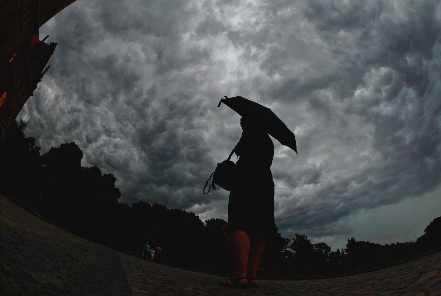 Eine Frau mit Regenschirm beobachtet die dunklen Wolken am Himmel.